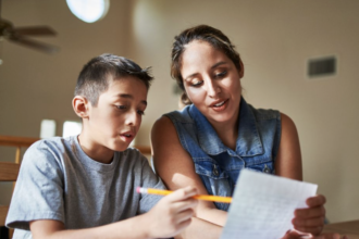 mother teaching her don to read while holding the paper.
